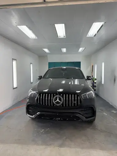A Mercedes-Benz SUV inside a lighted paint booth in the business listing photo